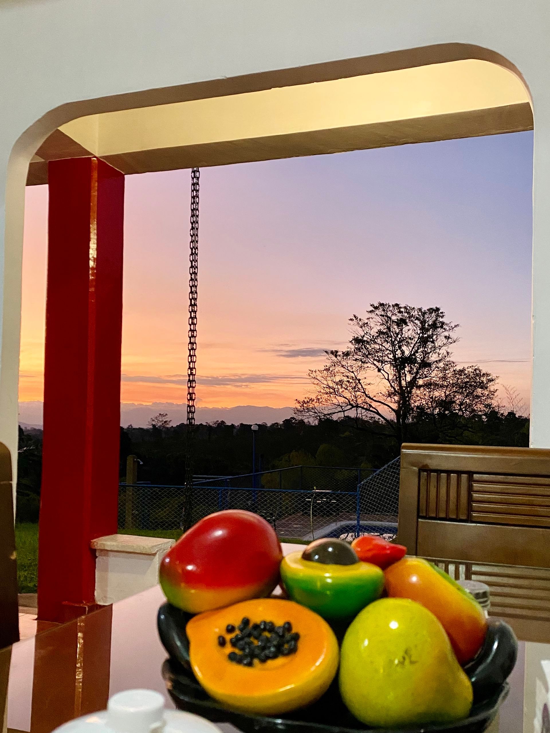 Un frutero sobre una mesa junto a un patio al aire libre al atardecer, con coloridas papayas y vistas al jardín.