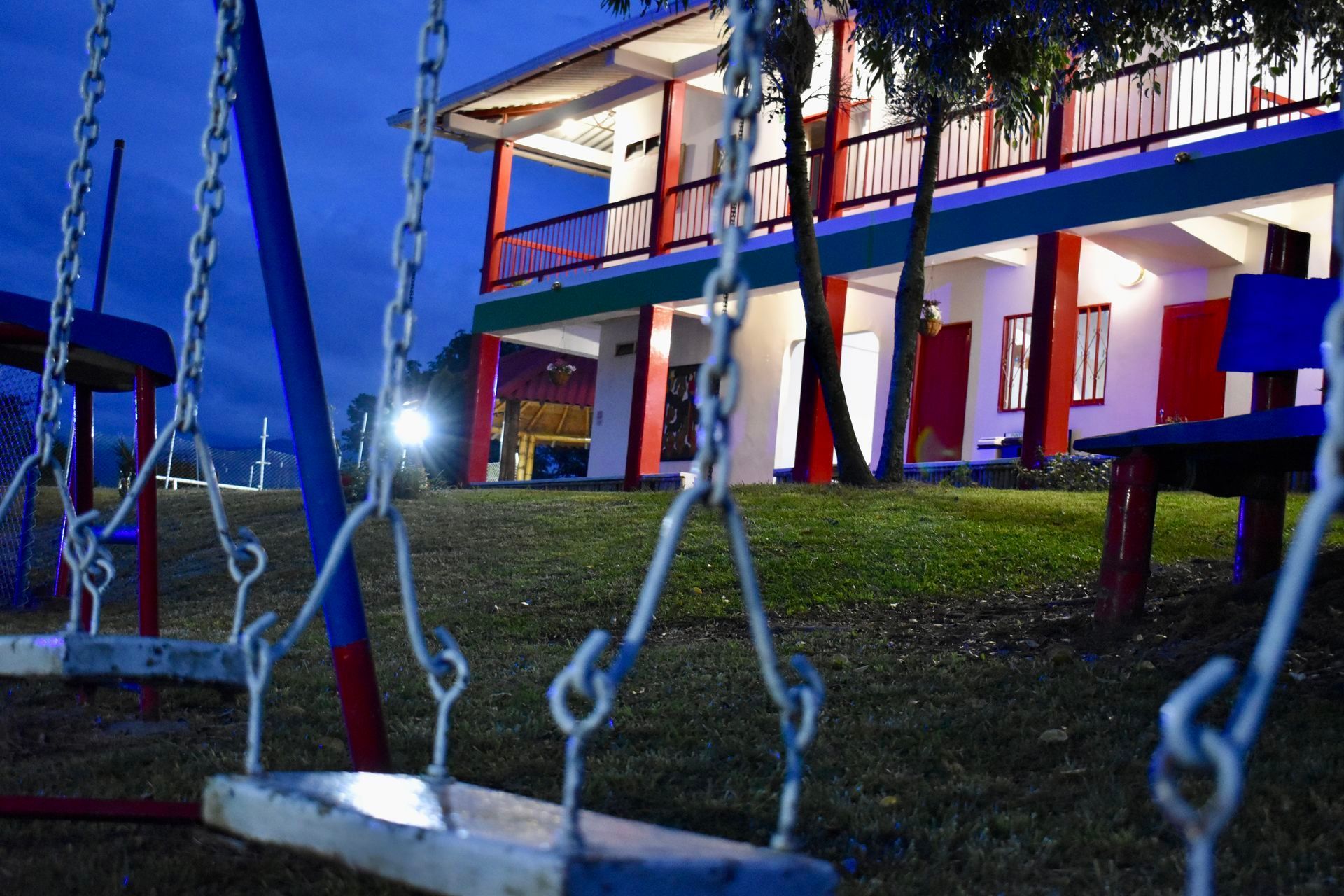 Cadenas de columpio en primer plano, con un edificio de dos pisos iluminado por la noche al fondo.