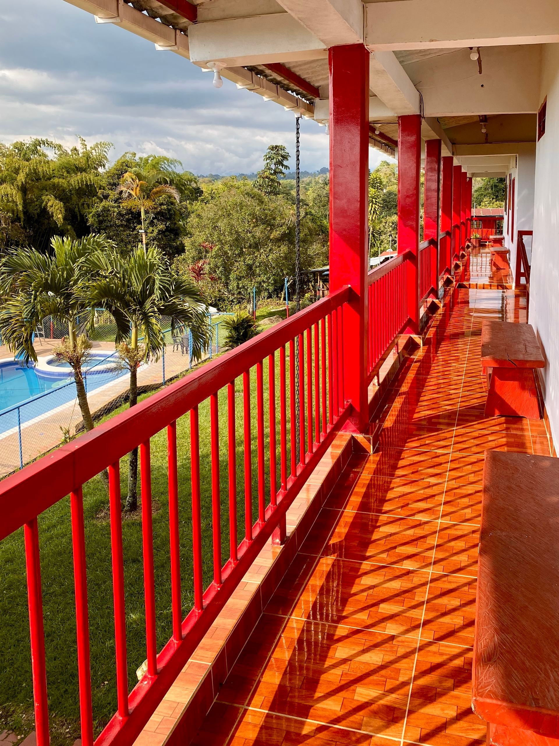 Pasarela con barandilla roja en el balcón con vistas a una piscina y un césped verde en un día soleado.