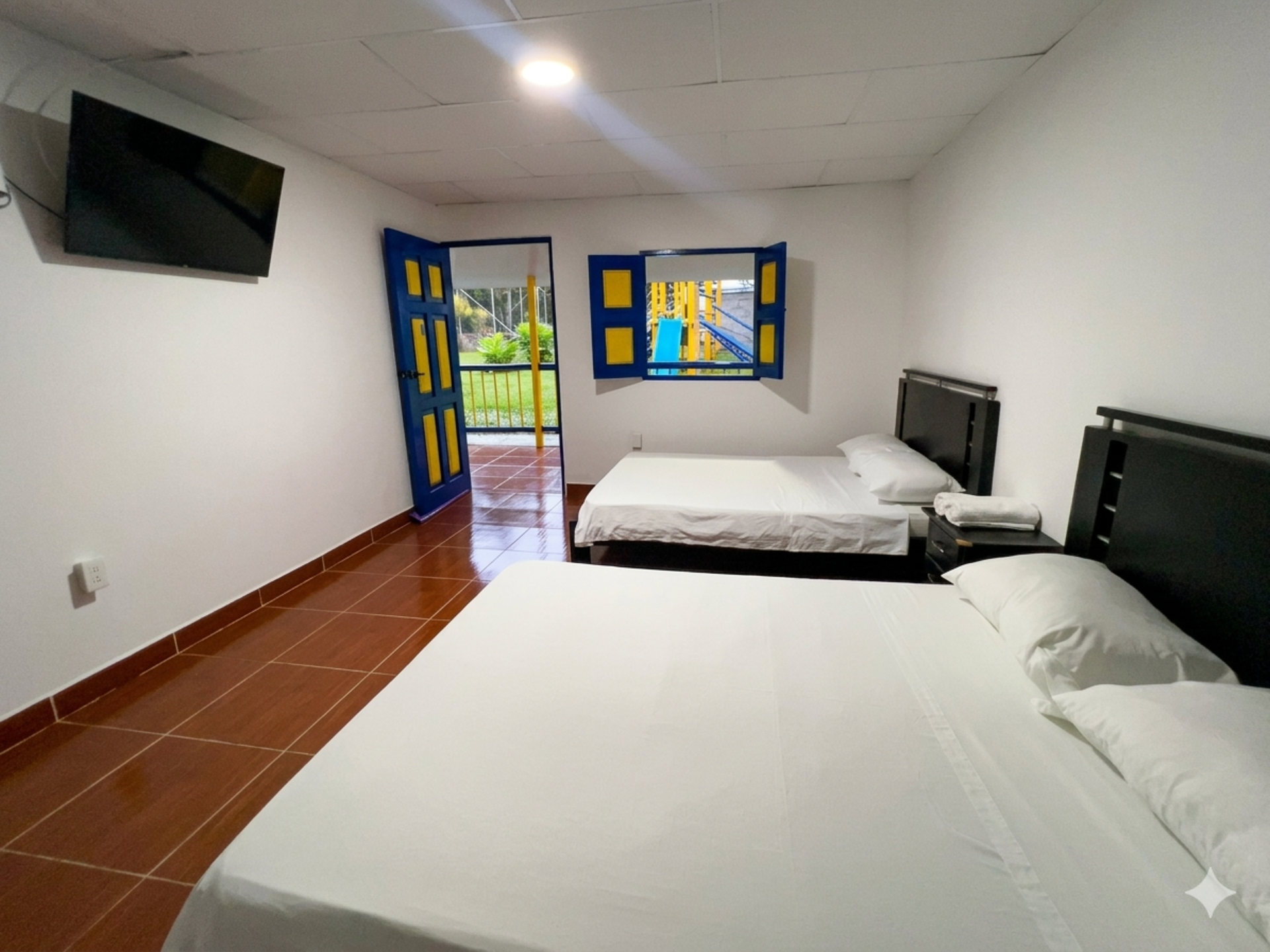 Habitación de hotel luminosa con dos camas, televisor montado en la pared