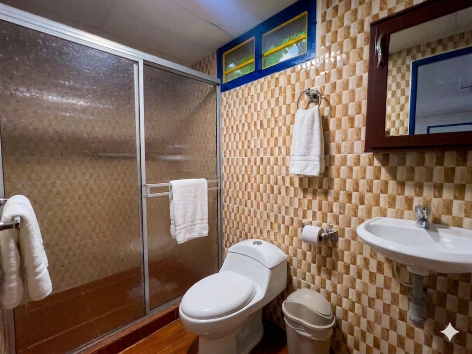 Baño accesible con ducha, inodoro, lavabo, barras de apoyo y paredes alicatadas en color beige.