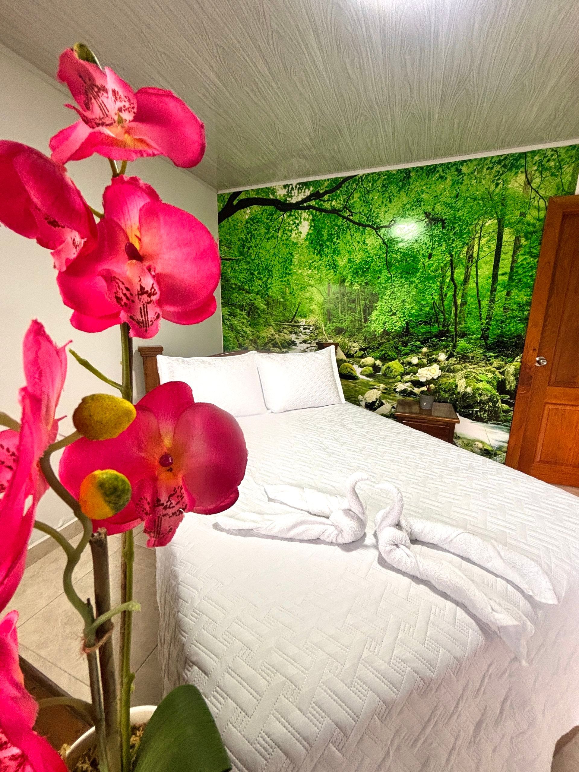 Orquídeas rosas en primer plano sobre una cama blanca con un mural de arte de bosque tropical.