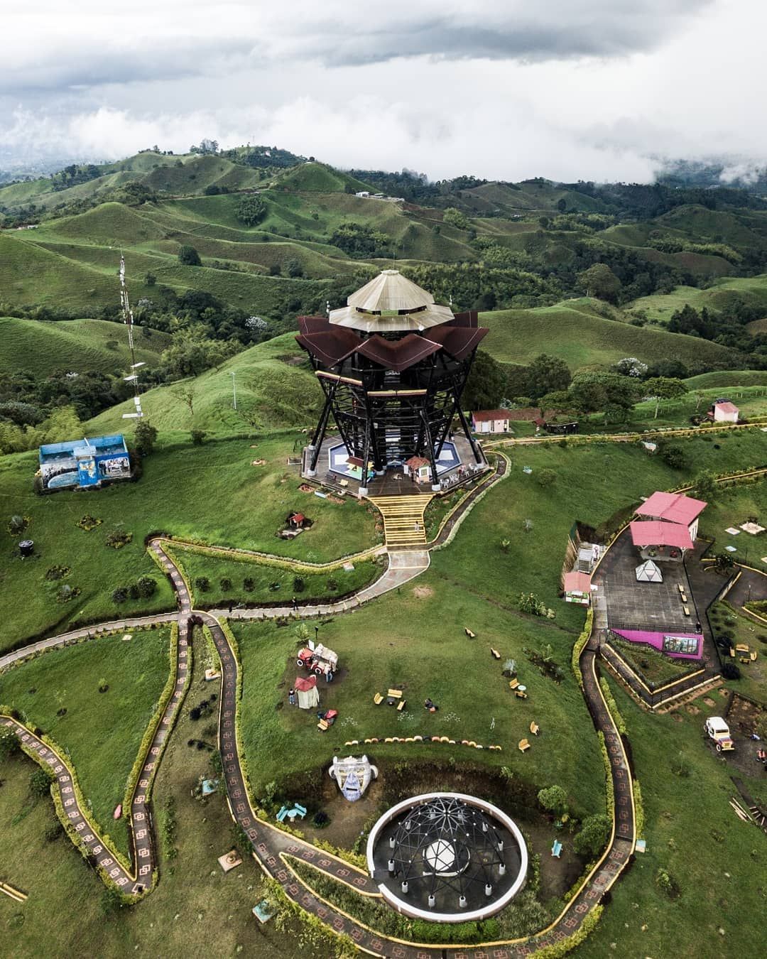 Mirador en la cima de una colina con una pagoda, senderos serpenteantes y verdes colinas onduladas bajo cielos nublados.