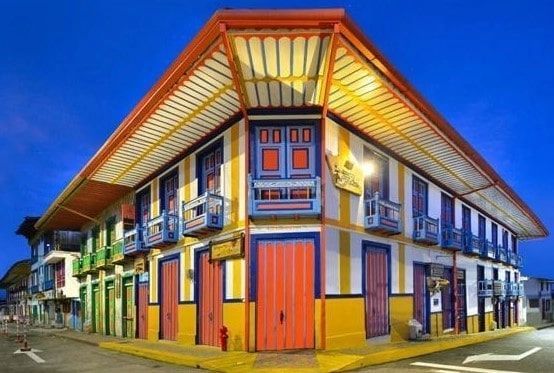 Edificio colorido en una esquina, con balcones, contraventanas brillantes y una puerta roja, al anochecer.