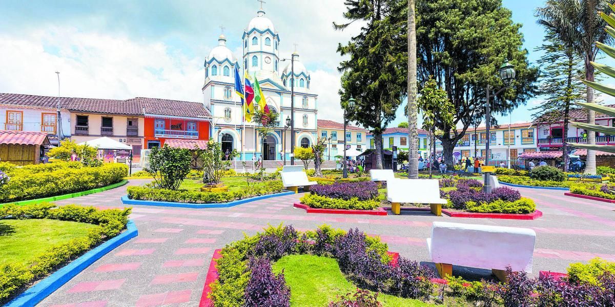 Un colorido jardín de flores con senderos sinuosos y una iglesia blanca al fondo.