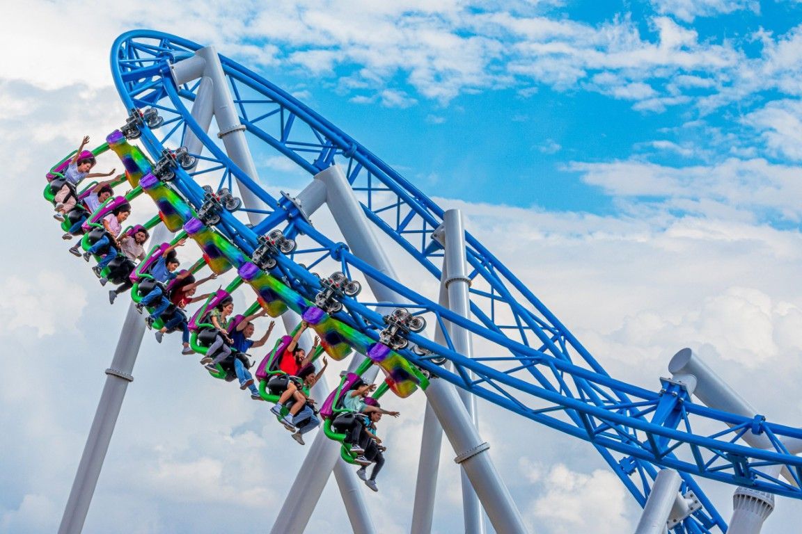 Un colorido tren de montaña rusa se balancea sobre una vía azul contra un cielo nublado.