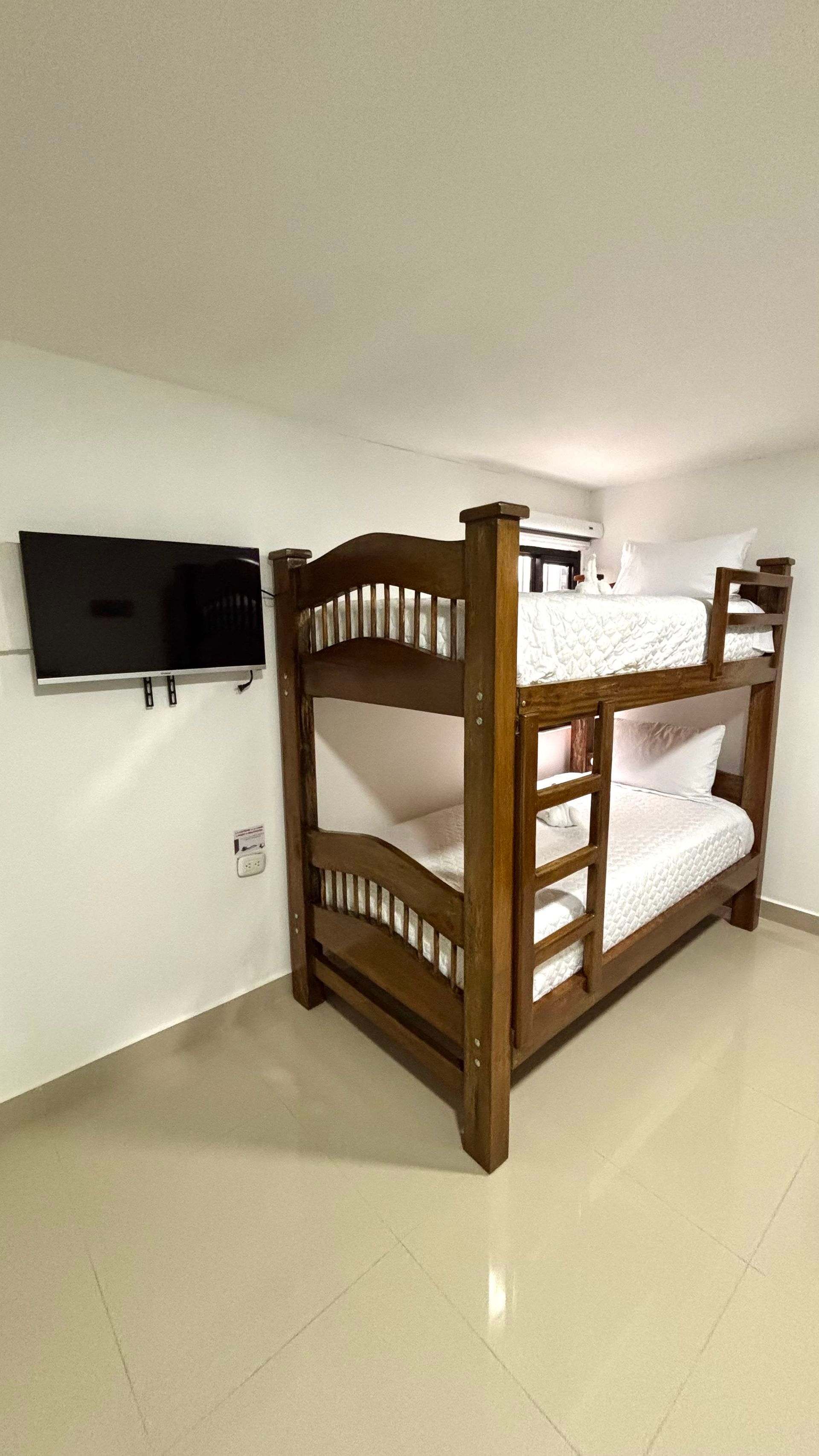 Litera de madera en un dormitorio minimalista con televisor montado en la pared y suelo de baldosas brillantes.