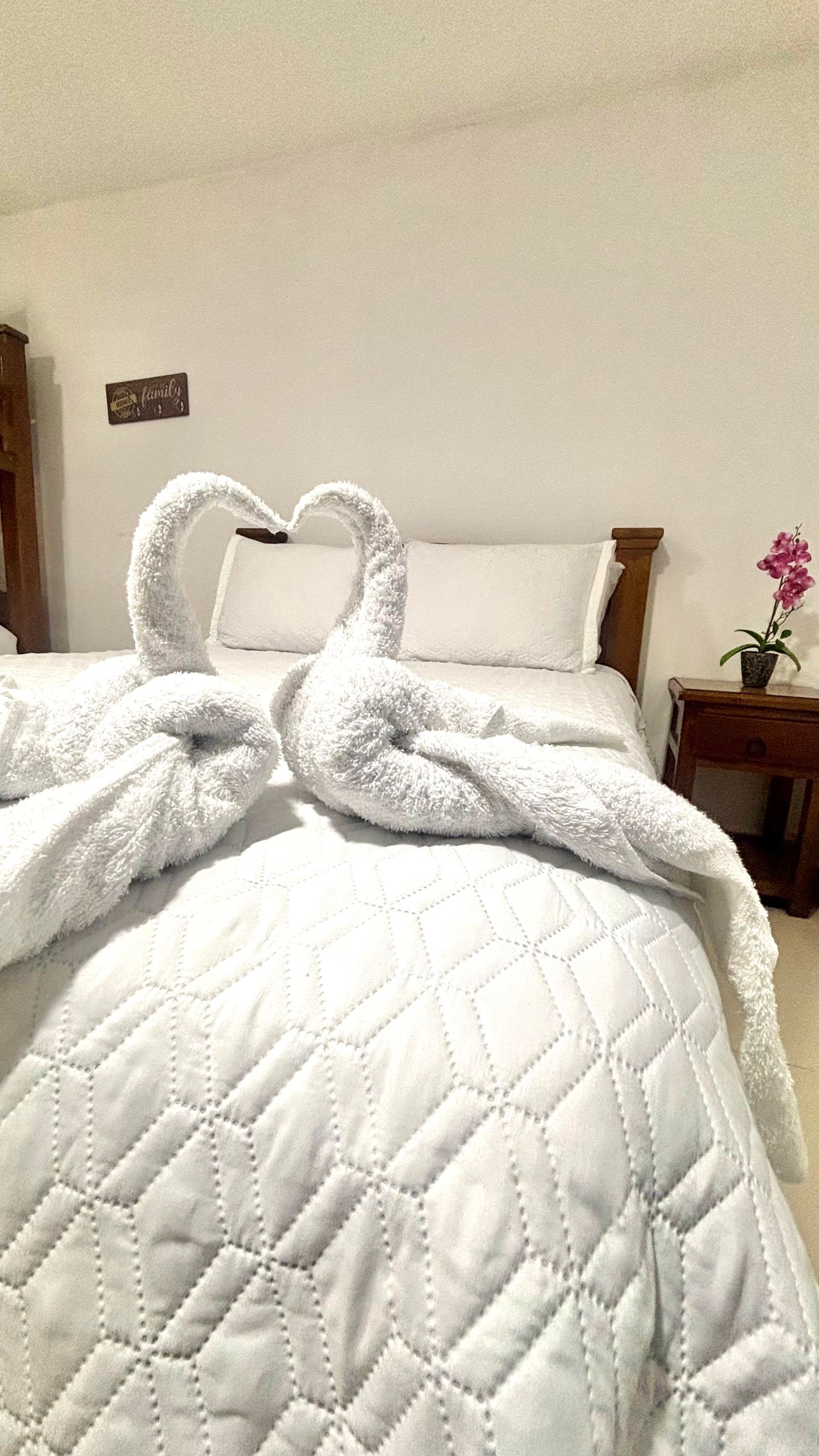 Cama bien hecha con edredón blanco y dos cisnes de toalla doblados en el piecero.