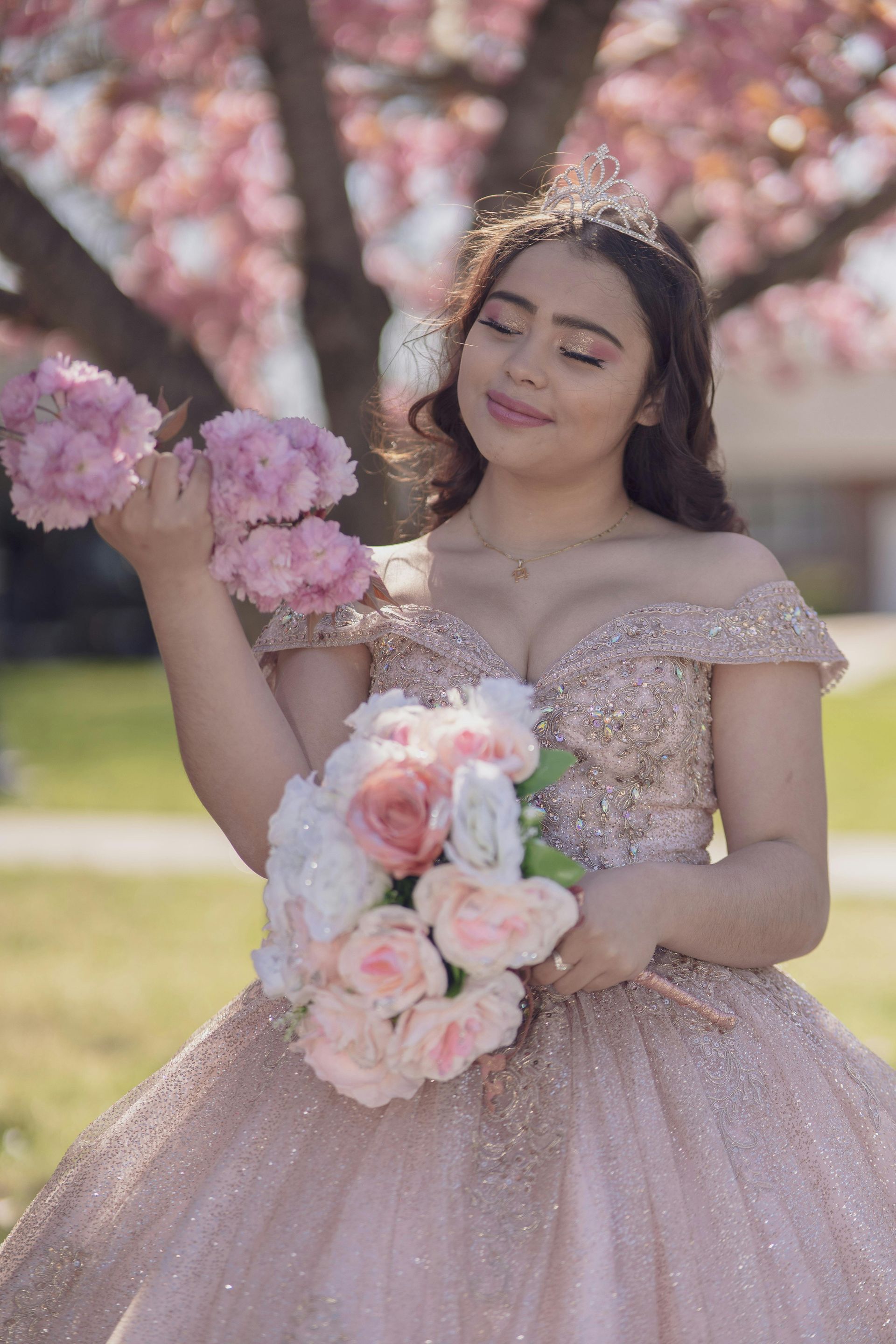 Mujer con vestido rosa sosteniendo un ramo de flores en tonos pastel bajo cerezos en flor.