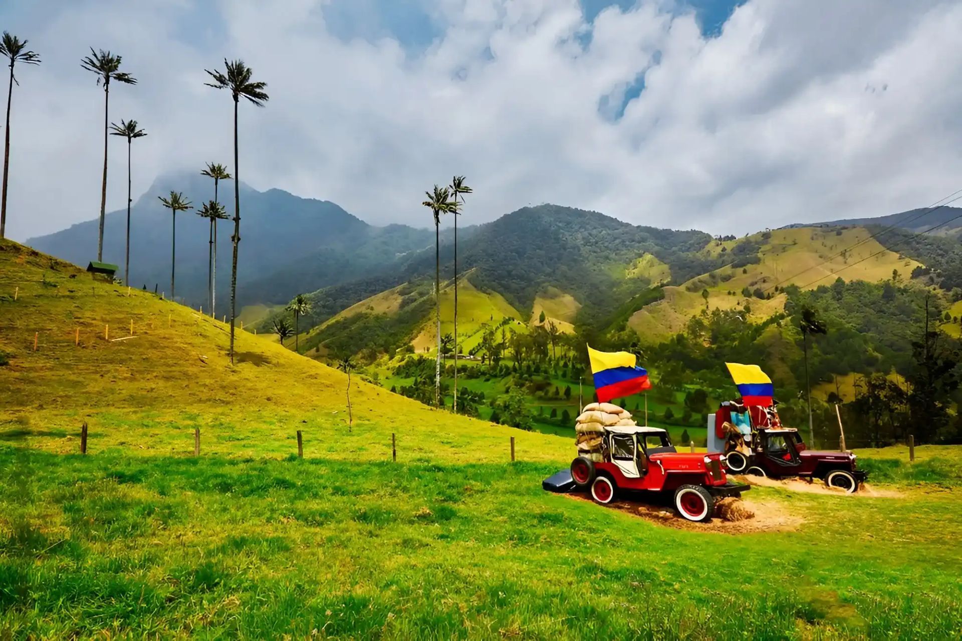 Dos jeeps rojos en un camino de montaña cubierto de hierba con banderas colombianas bajo un cielo nublado.