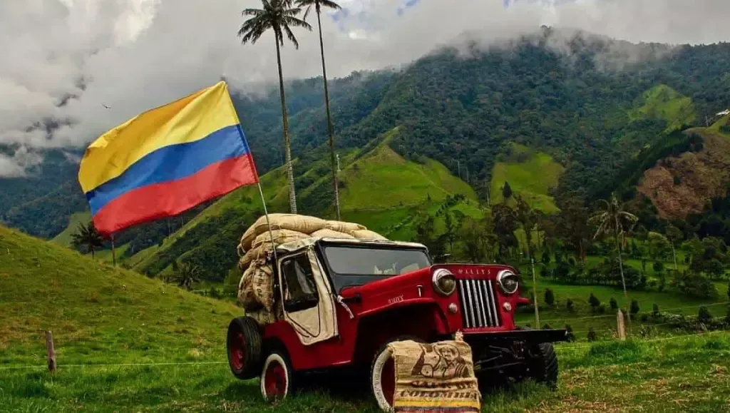 Jeep rojo en un valle de montaña verde con una bandera colombiana ondeando a su lado.