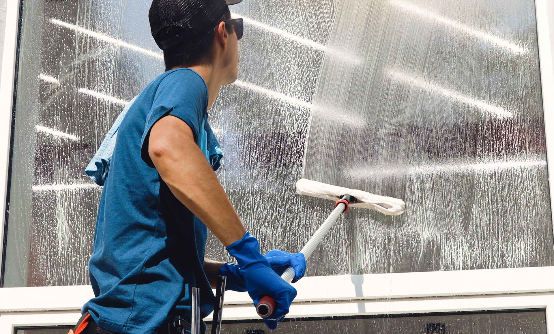 Person spraying a window with cleaning solution while wiping it with a clean fabric to remove dirt.