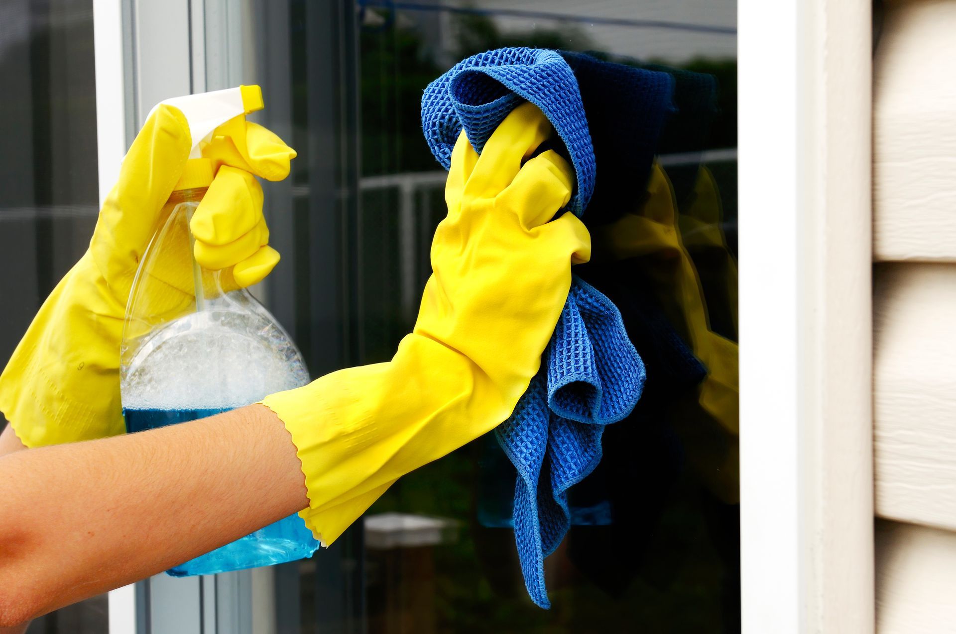 Person spraying a window with cleaning solution while wiping it with a clean fabric to remove dirt.