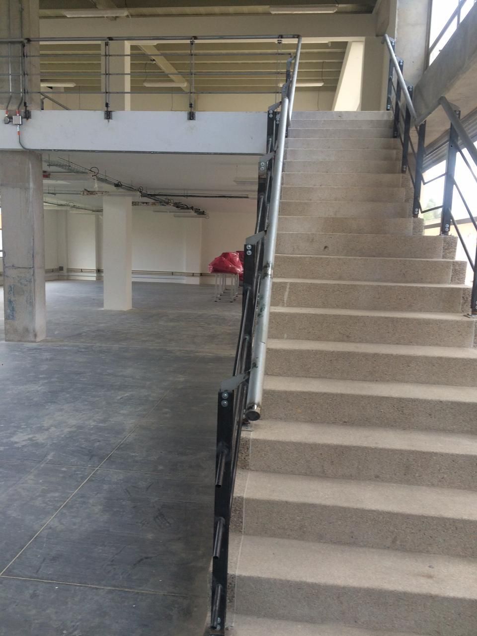 Escalera con barandilla negra que conduce al nivel superior. Fotografía interior de una estructura de hormigón.