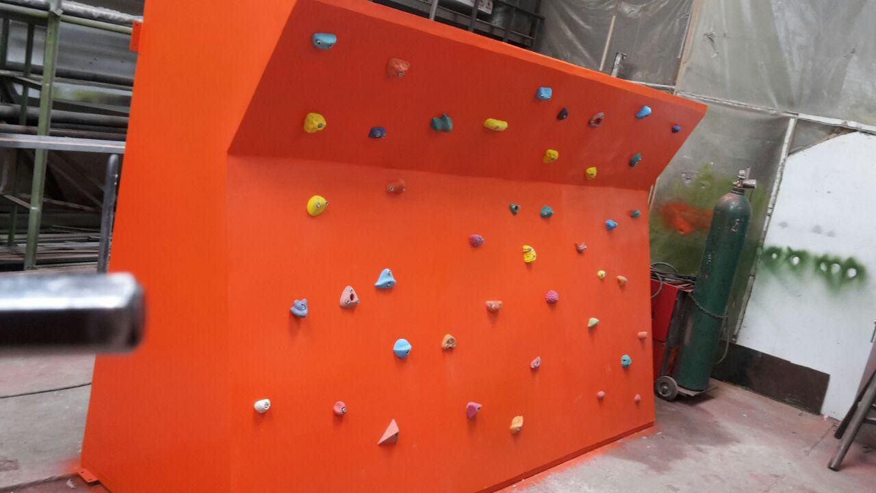 Muro de escalada de color naranja con asideros multicolores, situado en el interior.