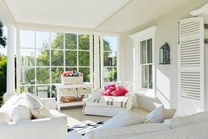 Bright, airy sunroom featuring white sofas, a matching console table, and pink decorative pillows.