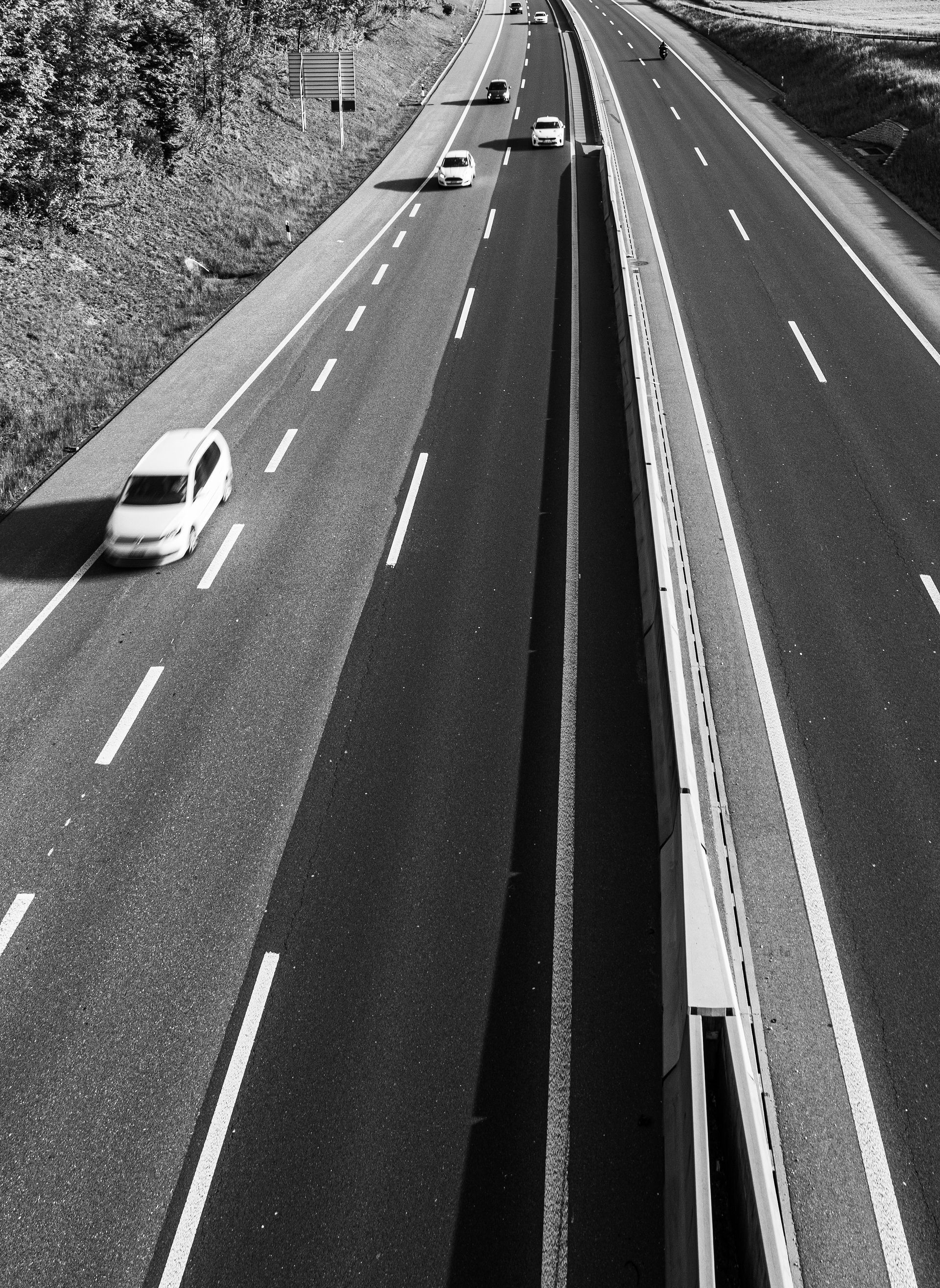 A black and white photo of a highway with cars on it.