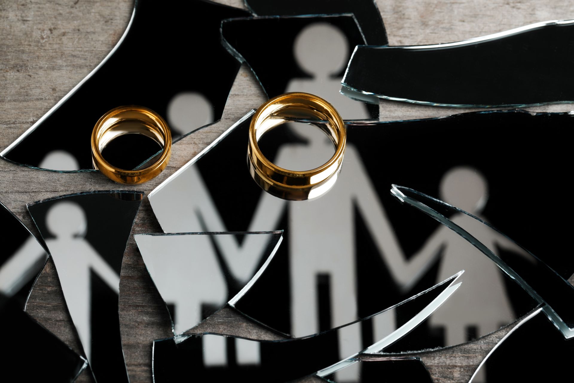 Wedding rings on shattered mirror pieces reflecting stick-figure family silhouettes.