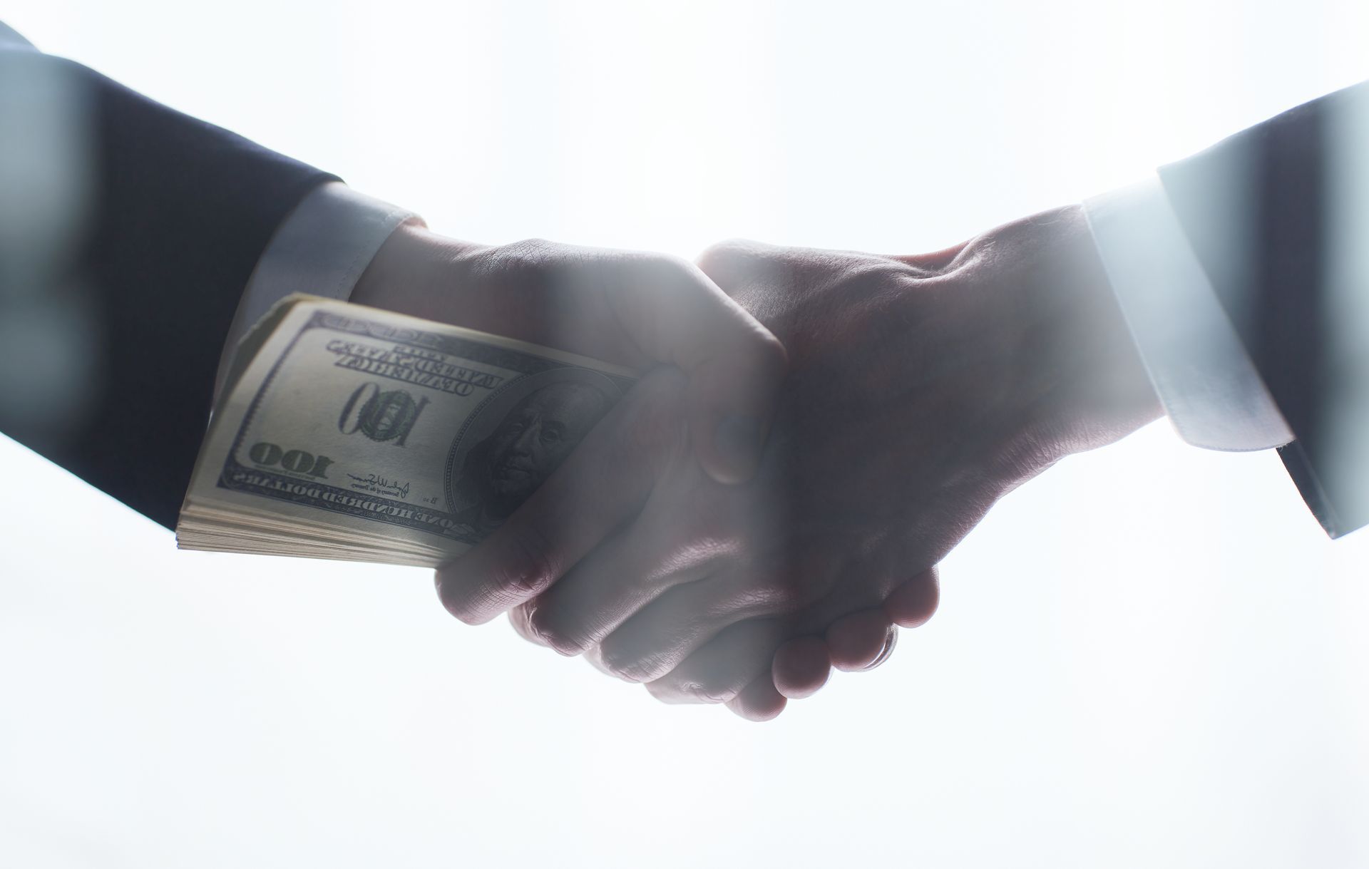 Hands shaking over a stack of cash, likely a Business Transactions Attorney in Draper