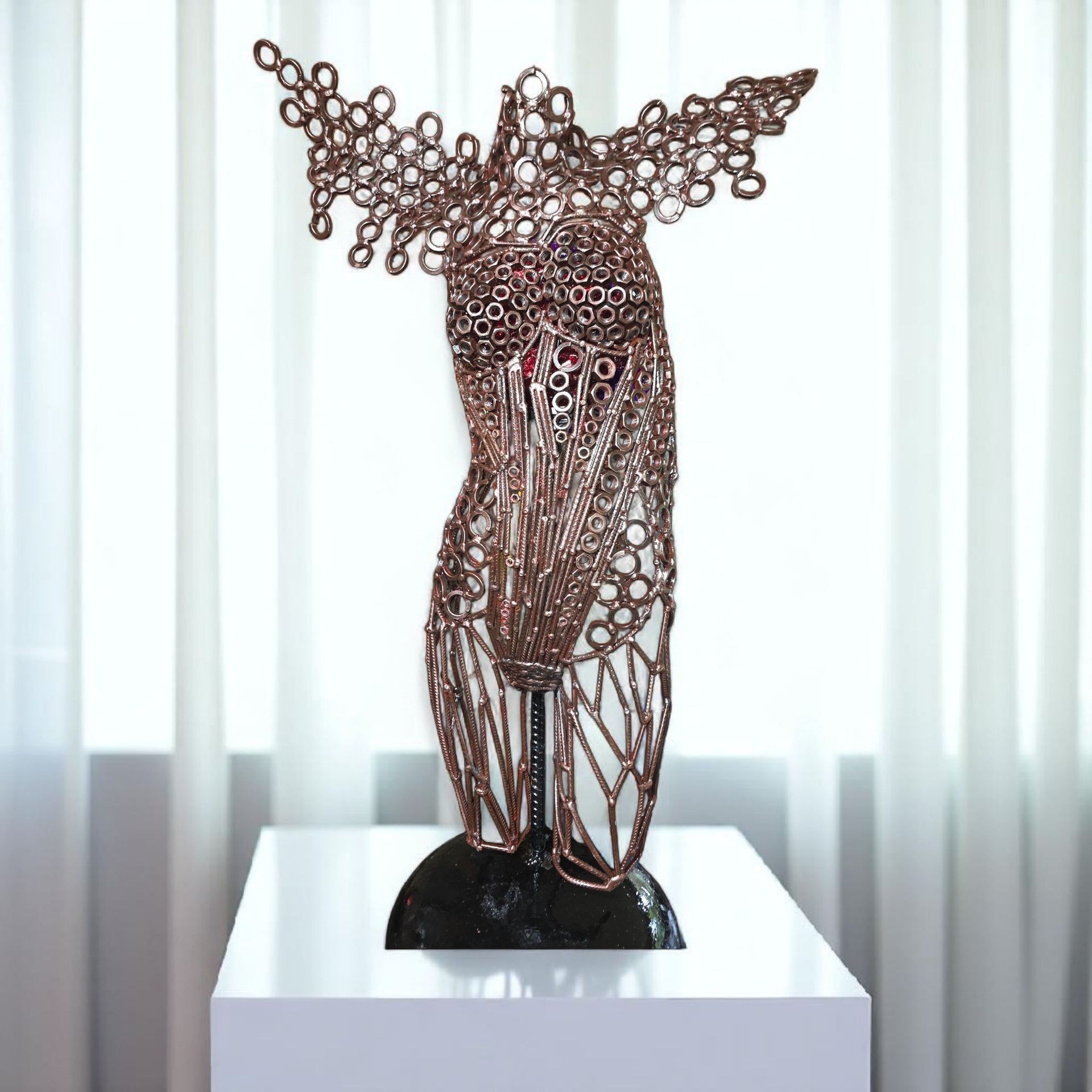 Copper wire sculpture of a torso, set on a white pedestal in front of a window with white curtains.