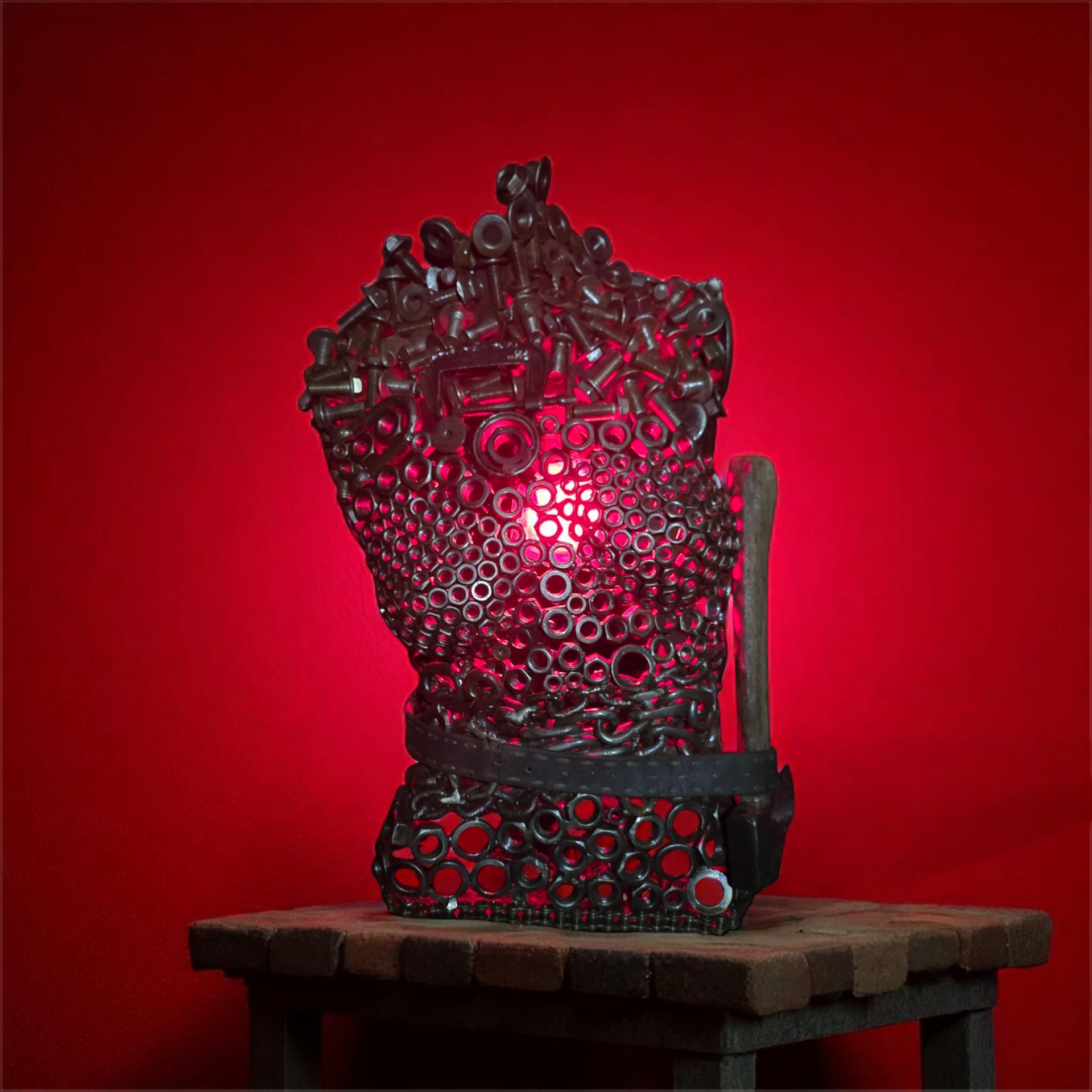 Metal sculpture lamp on wooden stand, red light inside, against a red backdrop.