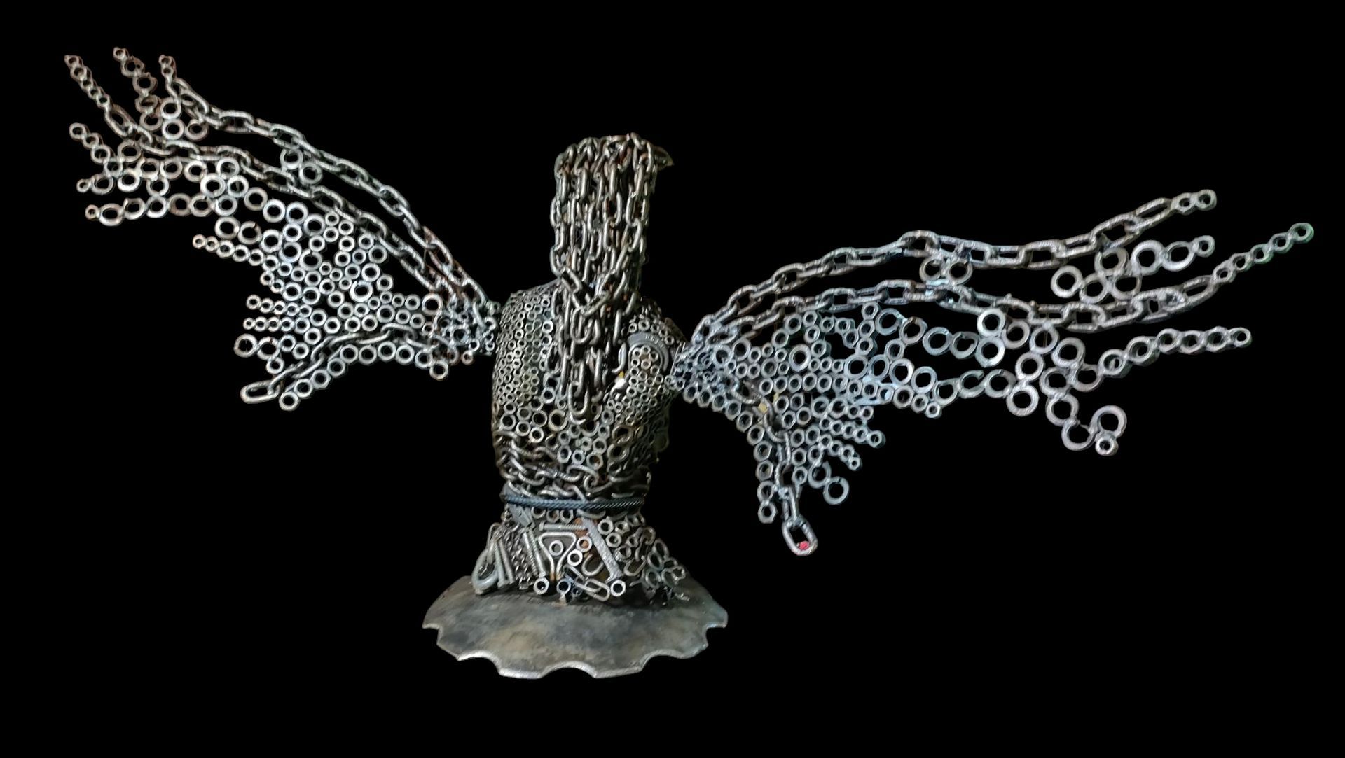 Sculpture of a figure with outstretched wings, constructed of metal chain links, set against a black background.