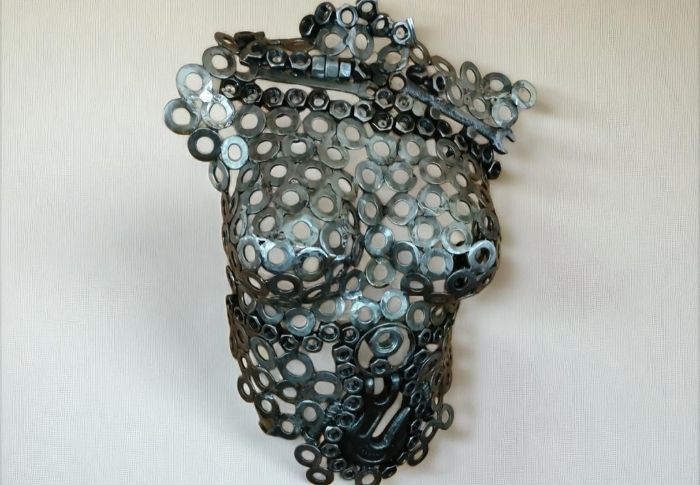 Metal sculpture of a torso made of washers, mounted on a plain, light-colored wall.