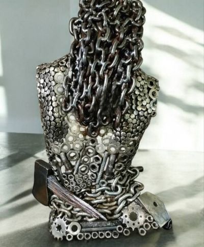 Metal sculpture of a person's bust, made from nuts, bolts, chains, and gears; gray and silver.