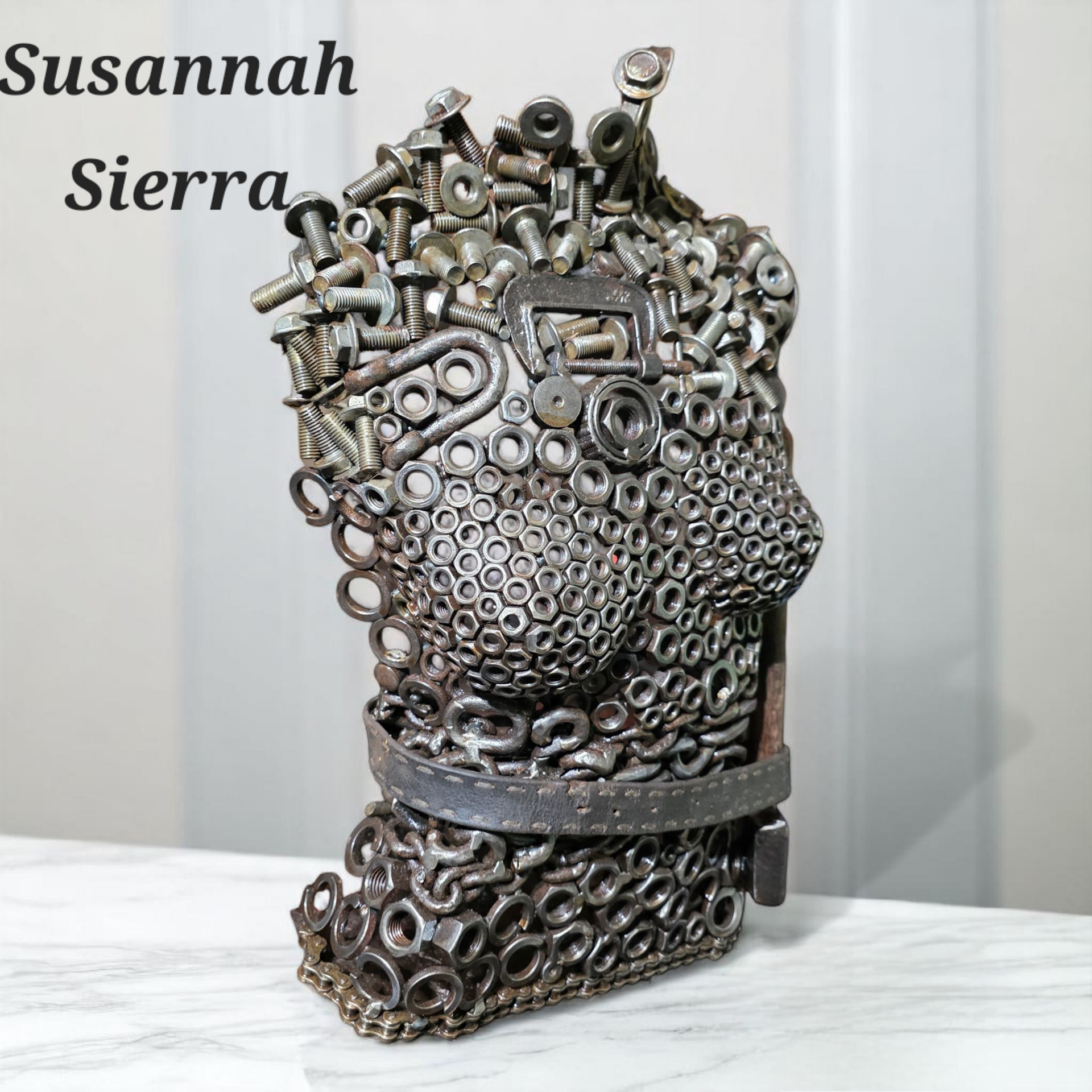 Sculpture of a head made from metal hardware, set on a white marble surface. 