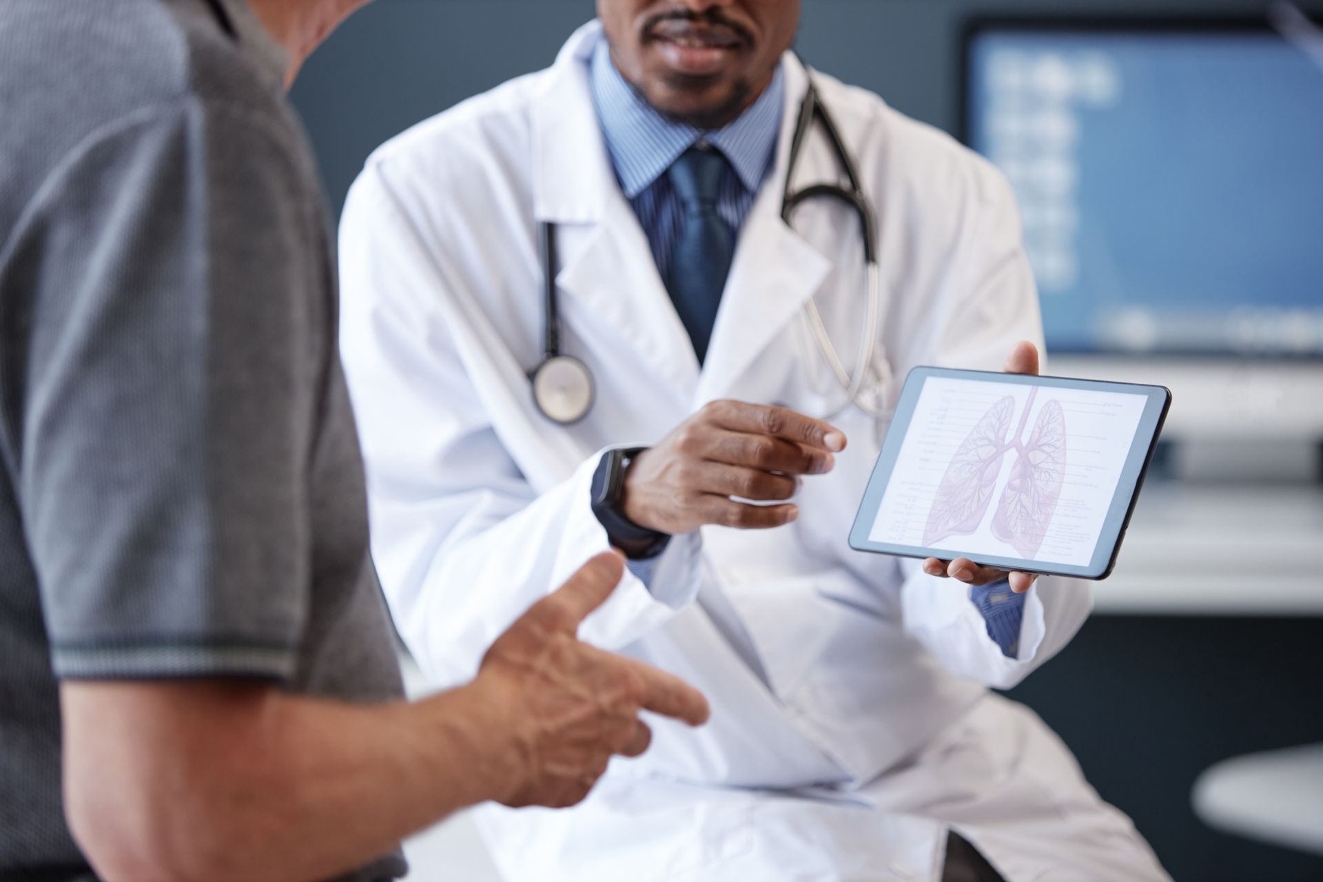 Doctor pointing to lung scan on a tablet, explaining to a patient in an office.