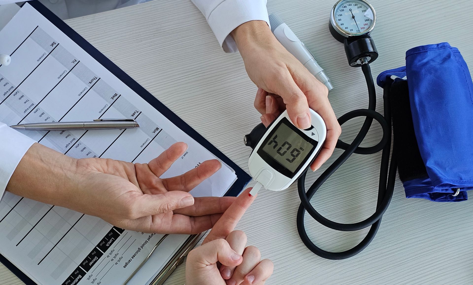 Person testing blood glucose with a meter; stethoscope and medical forms are nearby.