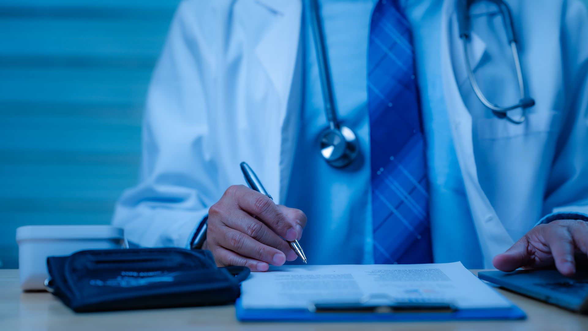 Doctor writing on clipboard, wearing white coat and stethoscope. Blue tones.
