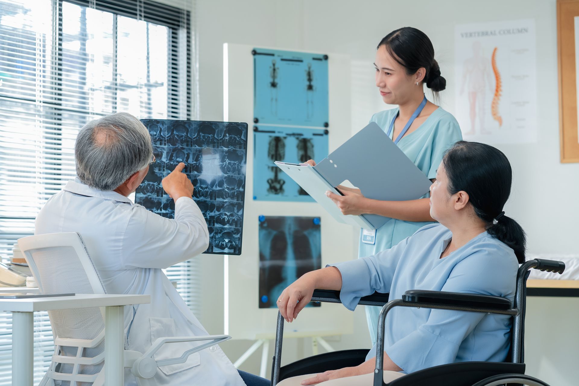 Doctor pointing at X-ray with a nurse and patient in a wheelchair in a medical office.