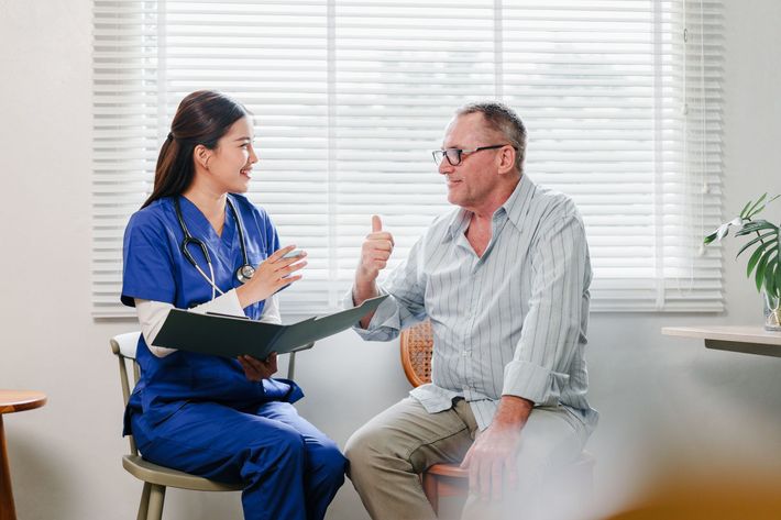 Nurse in blue scrubs consults with a patient in a well-lit room, patient giving a thumbs-up. Nurse in blue scrubs consults with a patient in a well-lit room, patient giving a thumbs-up.