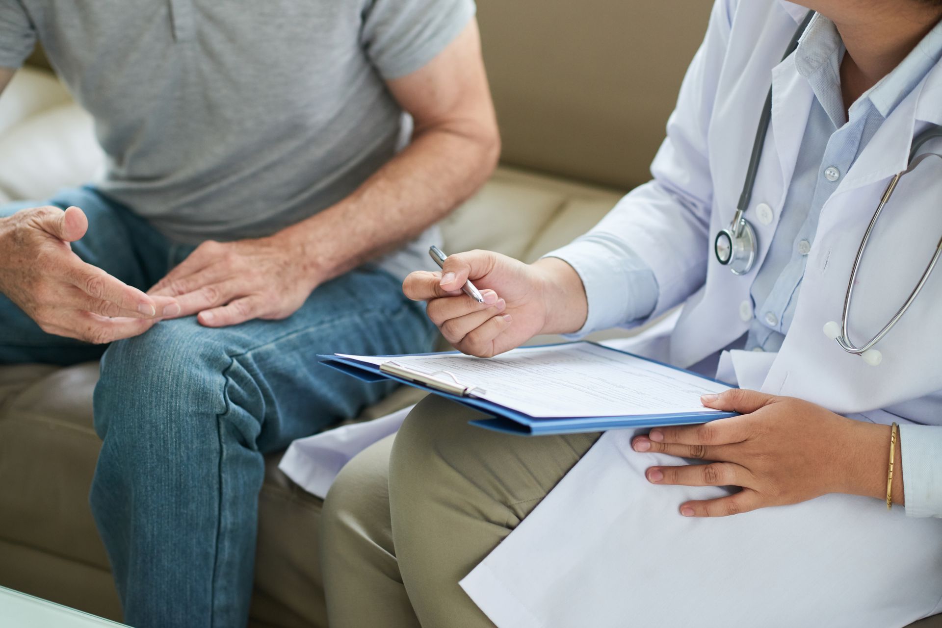 Doctor and patient discussing a medical chart; indoors. Doctor in lab coat holds chart and pen; patient gestures with hand. Doctor and patient discussing a medical chart; indoors. Doctor in lab coat holds chart and pen; patient gestures with hand.