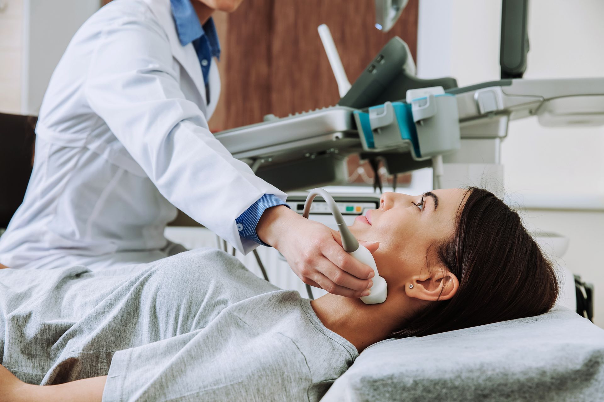Doctor performing ultrasound on a patient's neck with an ultrasound machine.