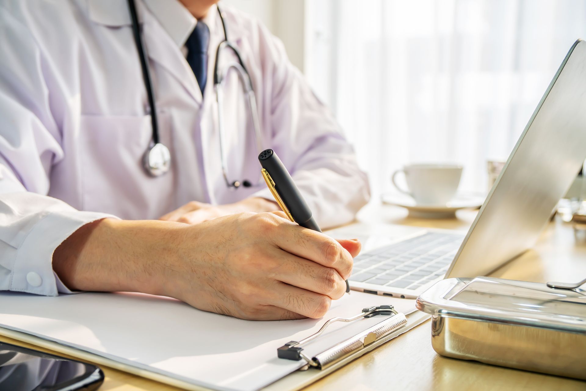 Doctor writing on a clipboard at a desk, laptop and stethoscope present. Doctor writing on a clipboard at a desk, laptop and stethoscope present.