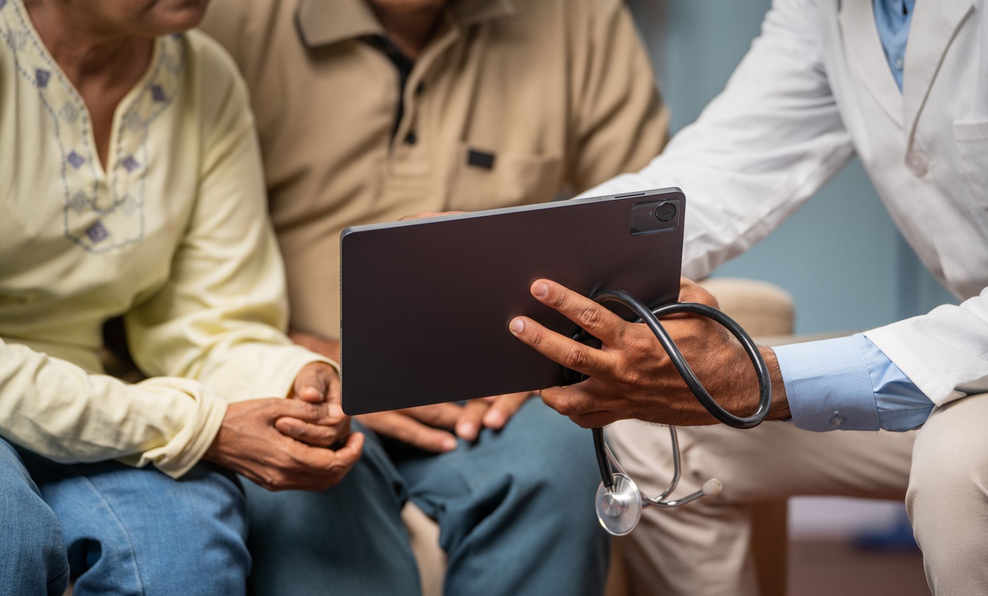 Doctor showing tablet to senior couple, stethoscope visible.