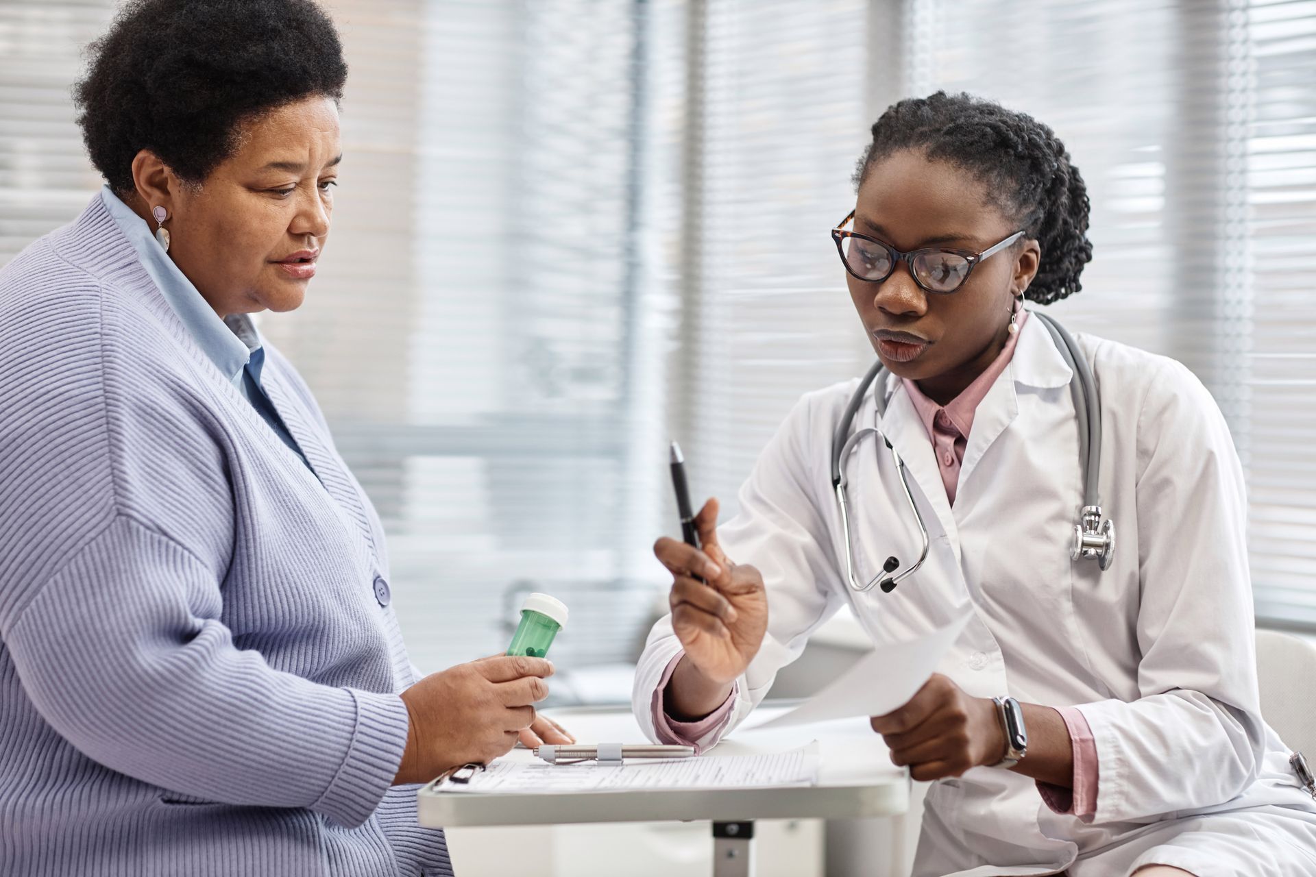 Doctor explaining medication to a patient in a medical office, holding a prescription and pen. Doctor explaining medication to a patient in a medical office, holding a prescription and pen.