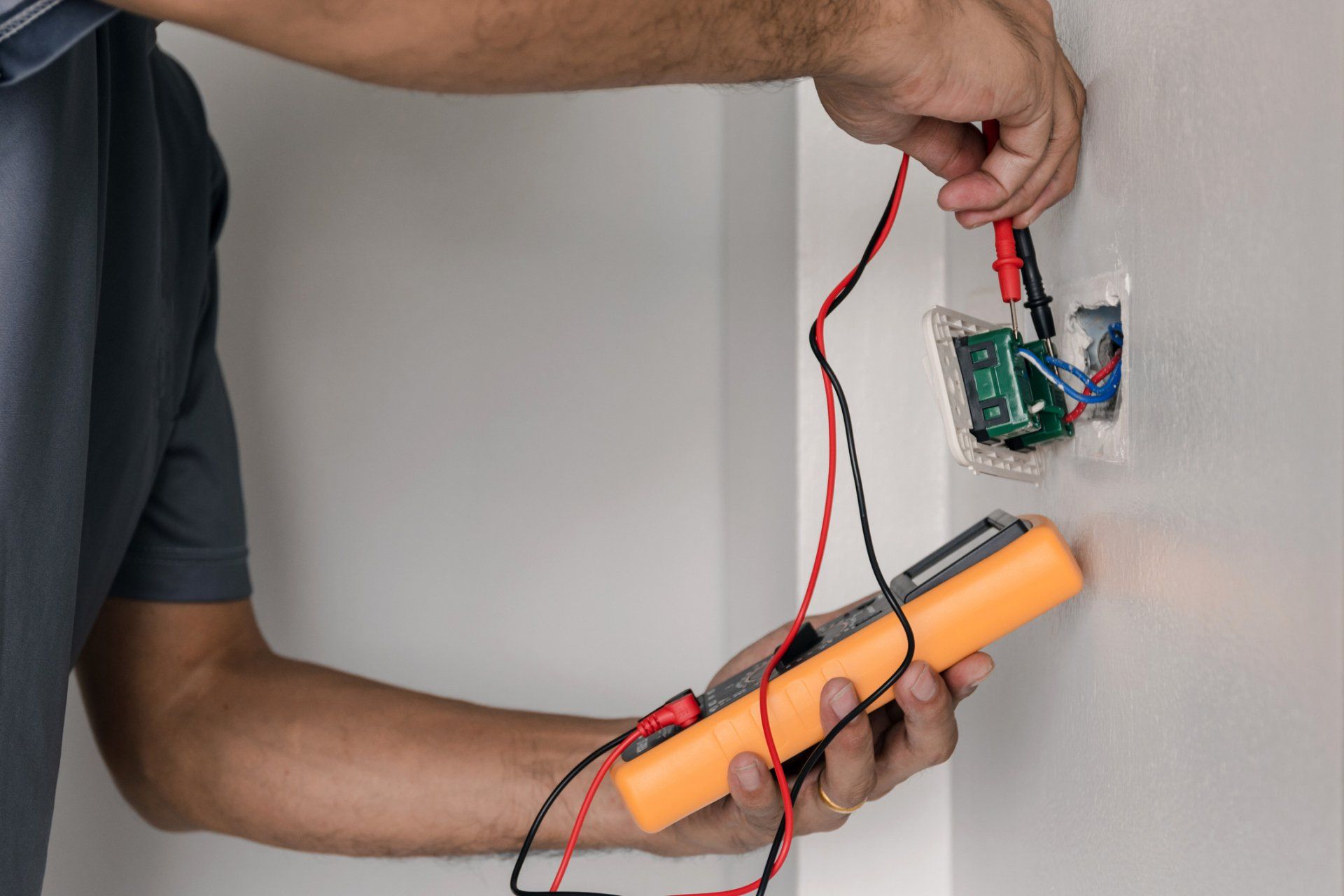 A man is using a multimeter to test a light switch on a wall.