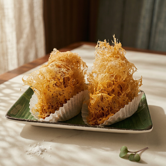 Two crispy, lacy, golden-brown deep-fried taro dumplings sit in paper liners on a rectangular green plate.