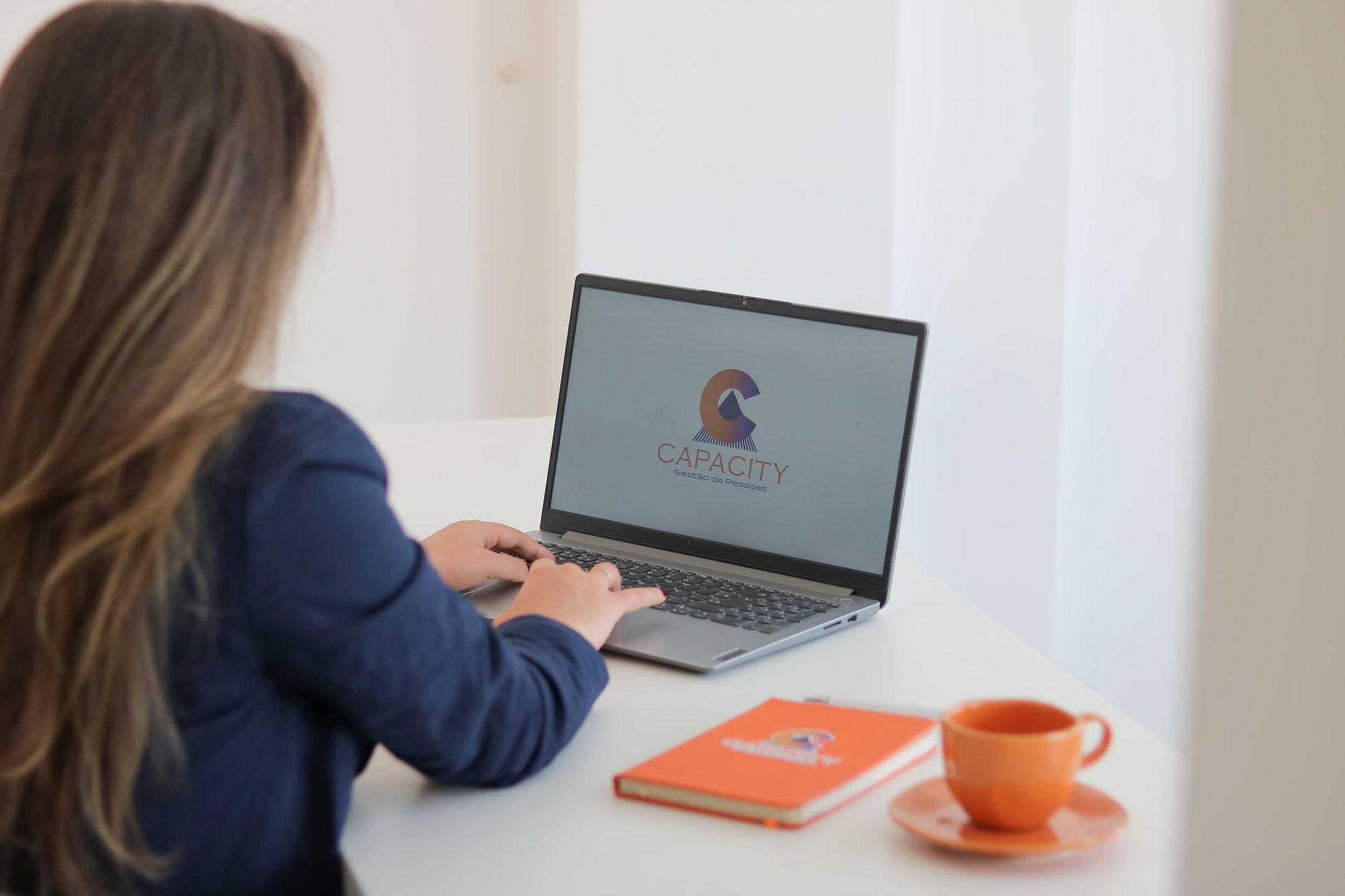 Uma mulher está digitando em um laptop com um logotipo de cavalo na tela