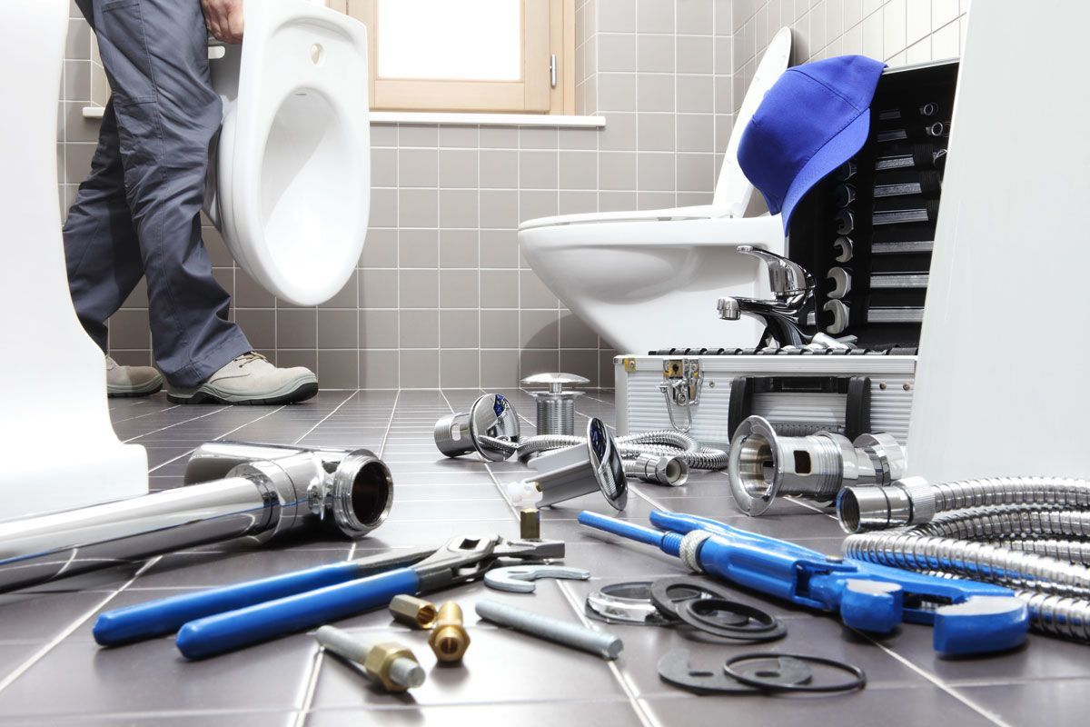 Plumber installing a toilet in a bathroom with tools scattered on the floor. Plumber installing a toilet in a bathroom with tools scattered on the floor.