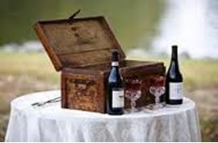 Open wooden chest on a white table with two wine bottles outdoors.