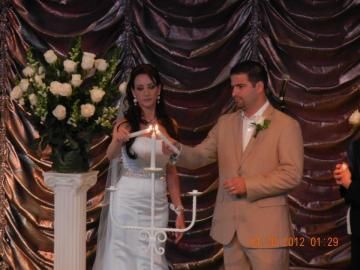 Bride and groom at a wedding ceremony, standing beside a decorated flower arrangement and curtain backdrop.