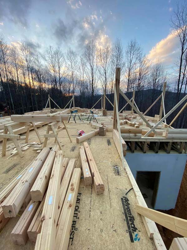Construction site, wooden framing for a house roof, against a cloudy sky.