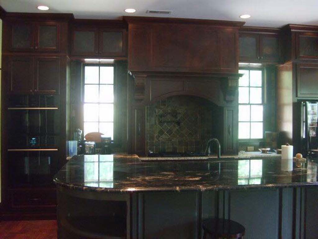 Dark wood kitchen with island, range hood, granite countertops, and windows.