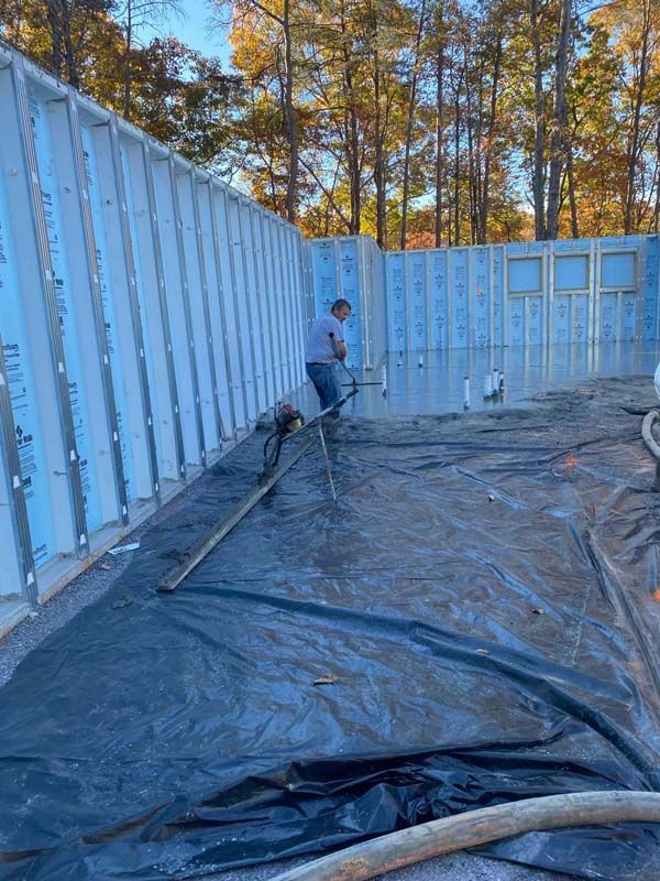 Man using a hose to spray concrete into a structure's foundation. Inside a partly built building with blue walls.