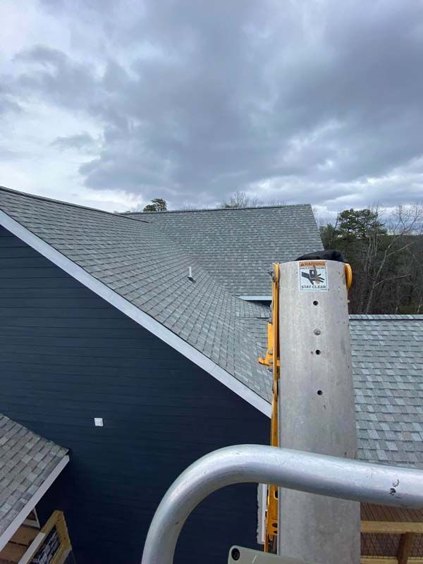 View of a shingled roof with a dark blue house exterior, cloudy sky, and a metal lift.