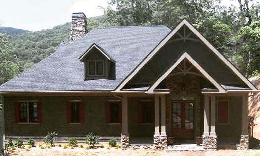 Green house with stone accents, gable roof, and small dormer. Set in a wooded landscape.